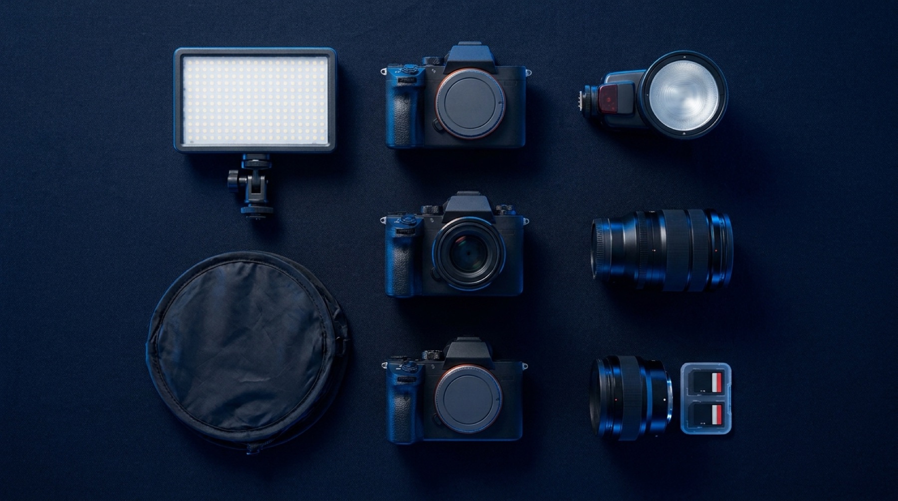 Câmeras, lentes, painel de LED e flash organizados sobre fundo escuro